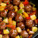 Ein Bild von Meatballs in einer Sauce, die aus einer Mischung aus Zwiebeln, Paprika, Pineapple und Zucker besteht.